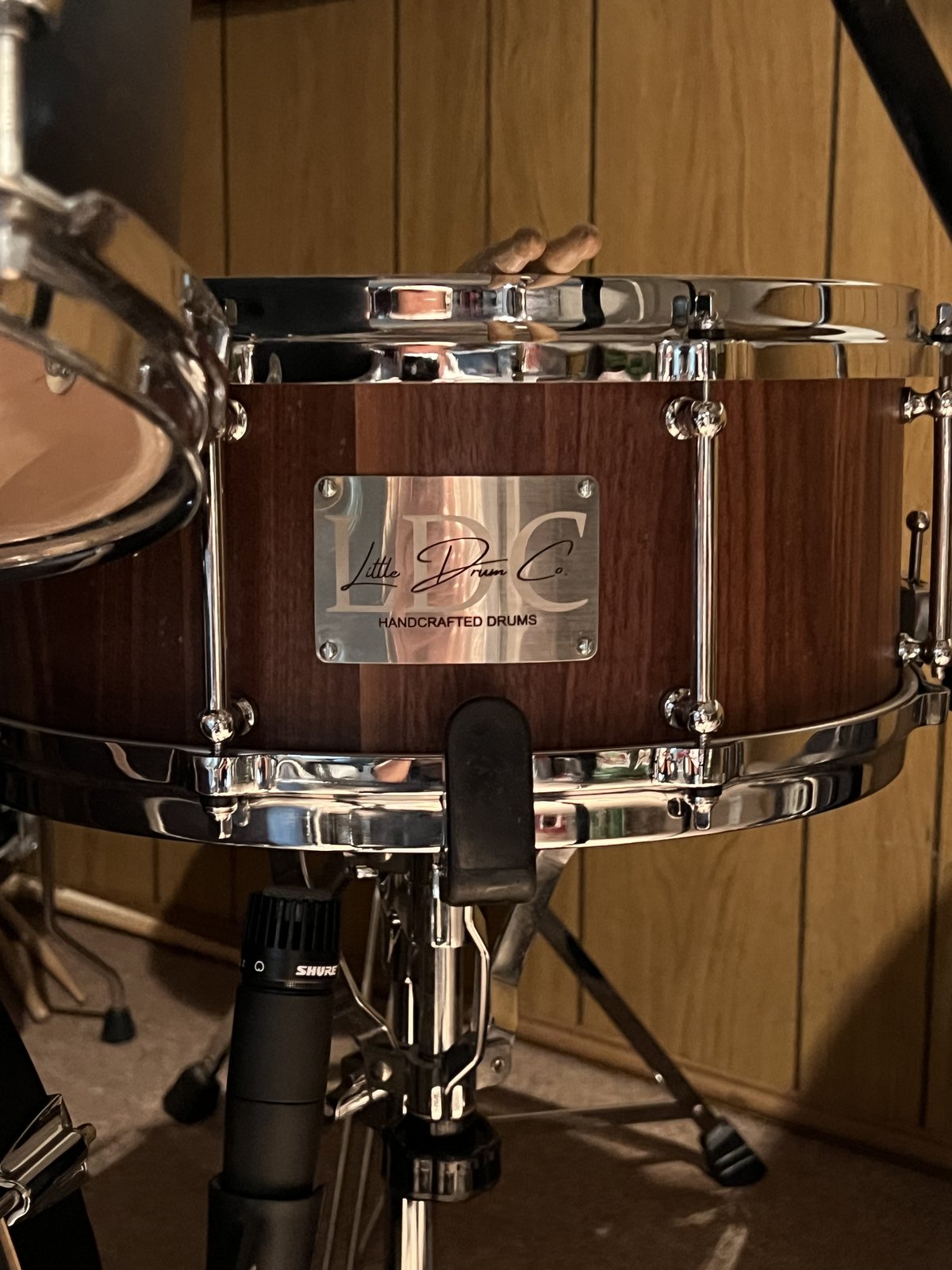 Dark hardwood stave snare drum with chrome hardware, mic'd up in the studio before shipping