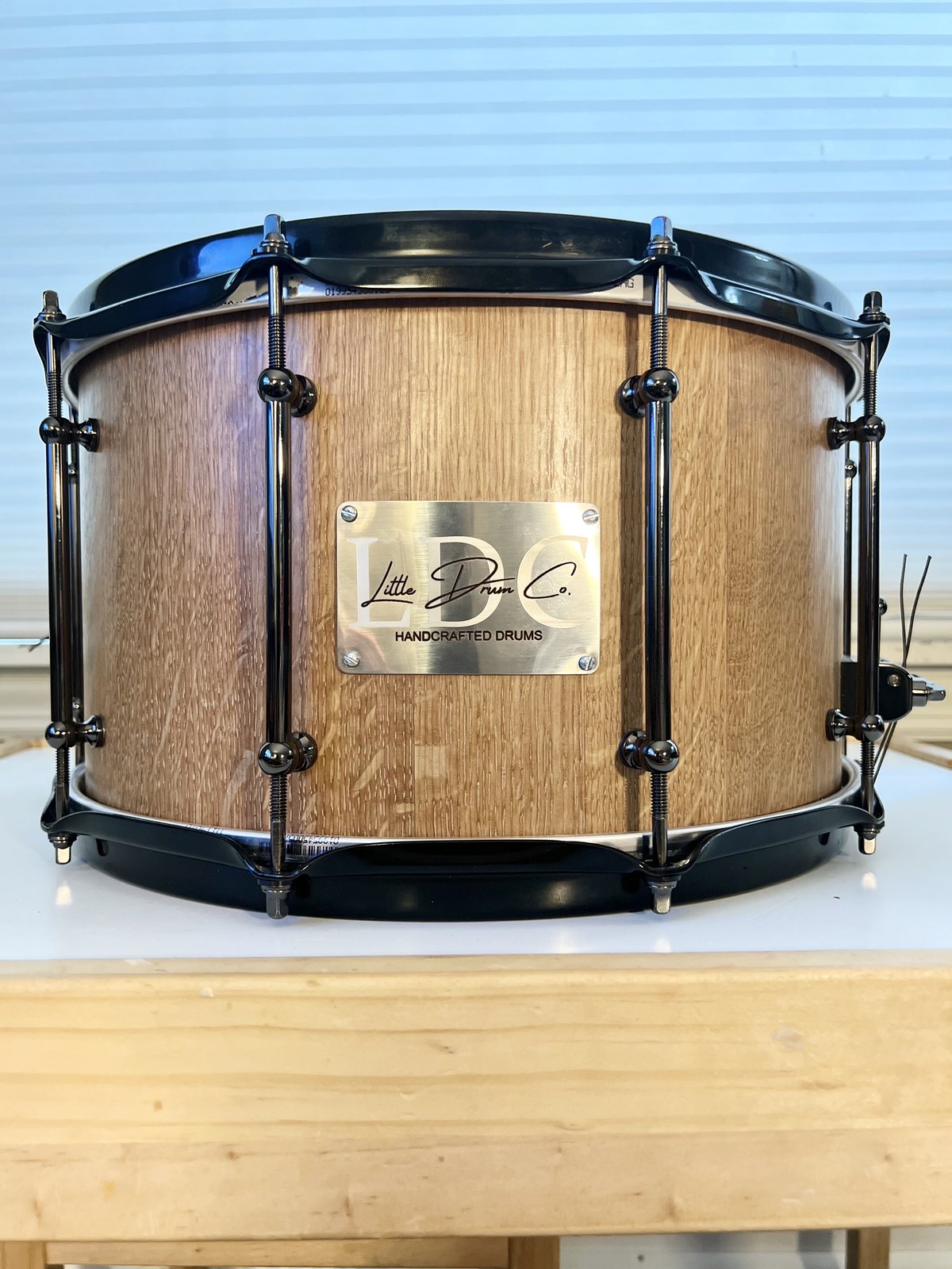 Quartersawn oak stave snare drum showing the ray fleck grain, with black hardware and a brushed LDC badge